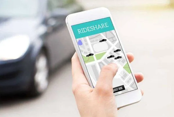 rideshare-accident-injury-attorney hand holding a cell phone with a rideshare app on screen and car in the background